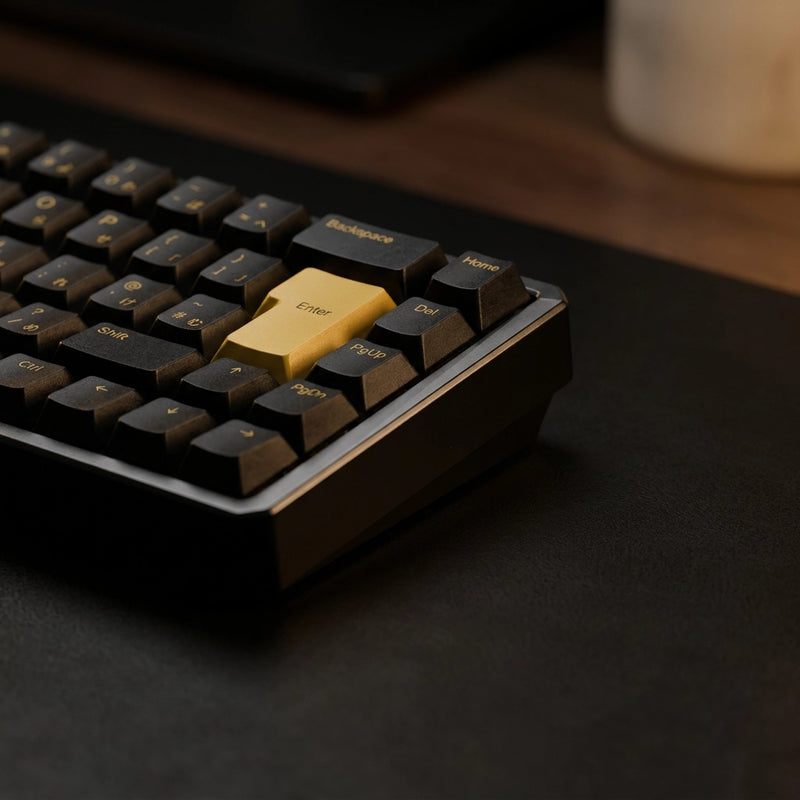 A close-up of a mechanical keyboard with black keycaps and a prominent gold power key, resting on a dark desk mat.