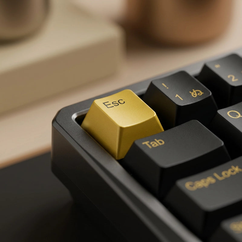 Close-up of a mechanical keyboard with a prominent gold Esc key surrounded by black keys with gold lettering, set against a warm blurred background.