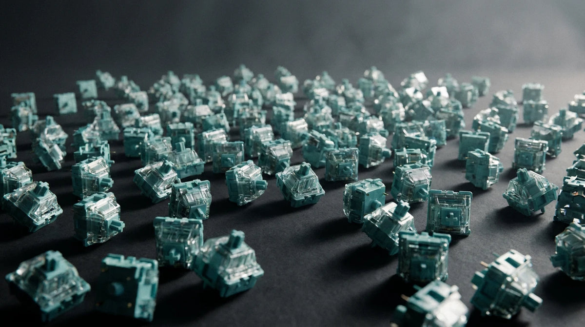 A close-up, shallow depth-of-field shot of numerous translucent teal mechanical keyboard switches scattered across a dark surface.
