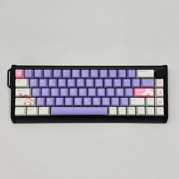 A compact mechanical keyboard with a black frame and a custom keycap layout. The keys are primarily light purple with white keycaps on the modifier keys and a pink keycap on the Enter key.