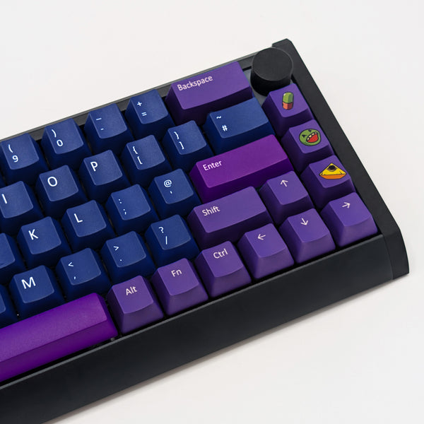 A close-up of a mechanical keyboard with custom keycaps. The keys feature a color-blocked design with dark blue keys on the left, purple modifier keys (Backspace, Enter, Shift, Alt), and a black keyboard frame with small colorful emoji-style key accents.